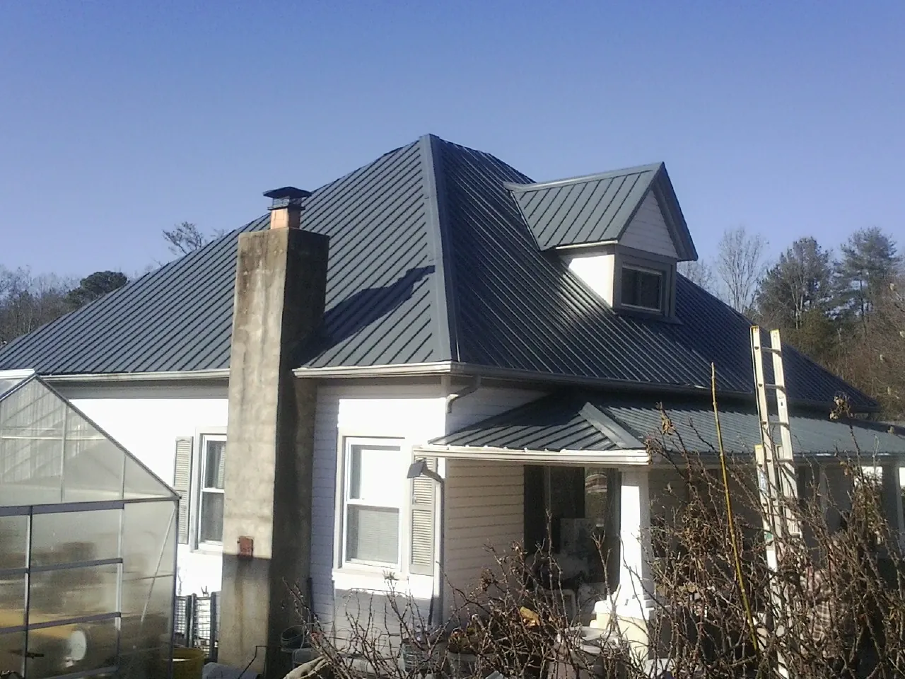 Dark blue standing seam metal roof on a white farmhouse with dormer — Slate & Tile Roof Repair by Roofing Brothers in Darien Center