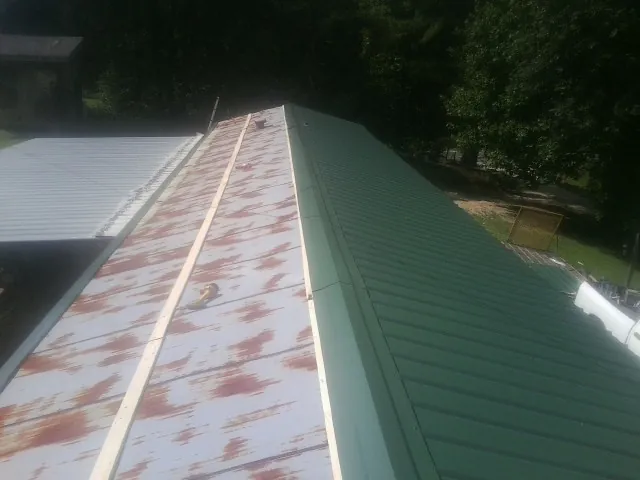 Old rusted panels beside newly installed green metal roofing — Wind Damage Roof Repair by Roofing Brothers in Darien Center