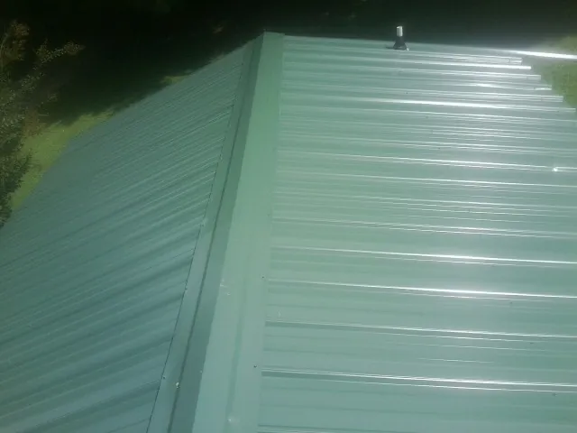 New green metal panels meeting at the ridge of a roof — Flat Roof Repair work by our crew in Darien Center