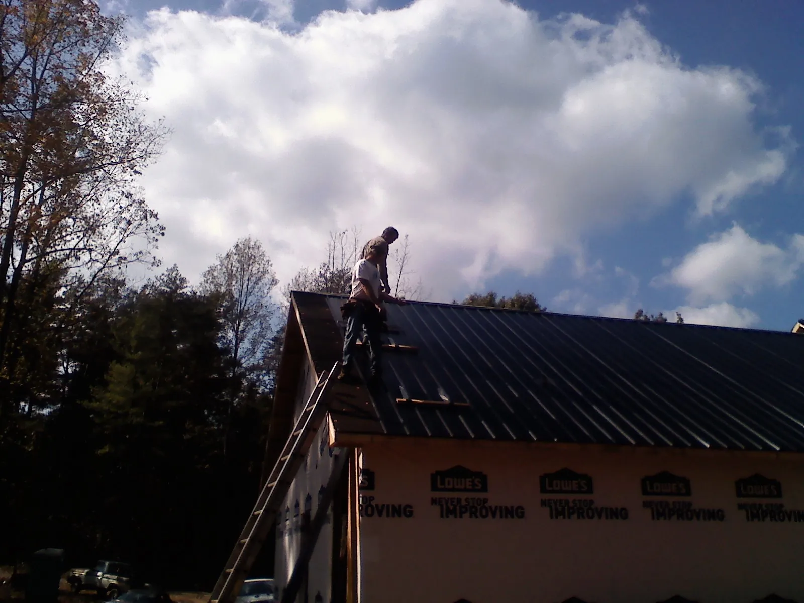Roofer fastening dark metal panels high against a cloudy sky, from a Roof Inspection job in Darien Center