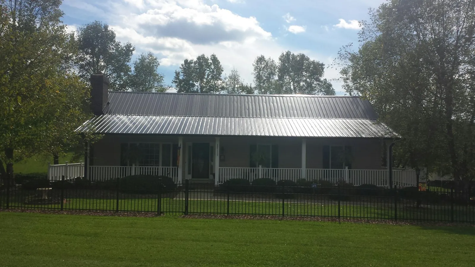 Gray metal roof on a brick ranch with a full width front porch — Gutter Guard Installation work by our crew in Darien Center