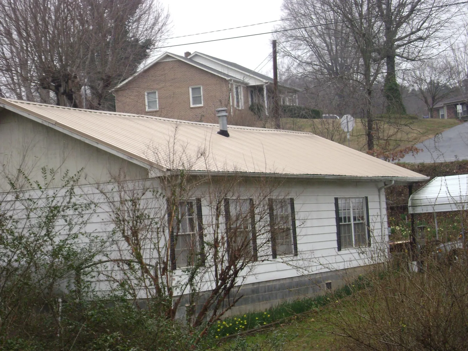 Tan metal roof on a white sided house set into a hillside — Commercial Roofing by Roofing Brothers in Darien Center