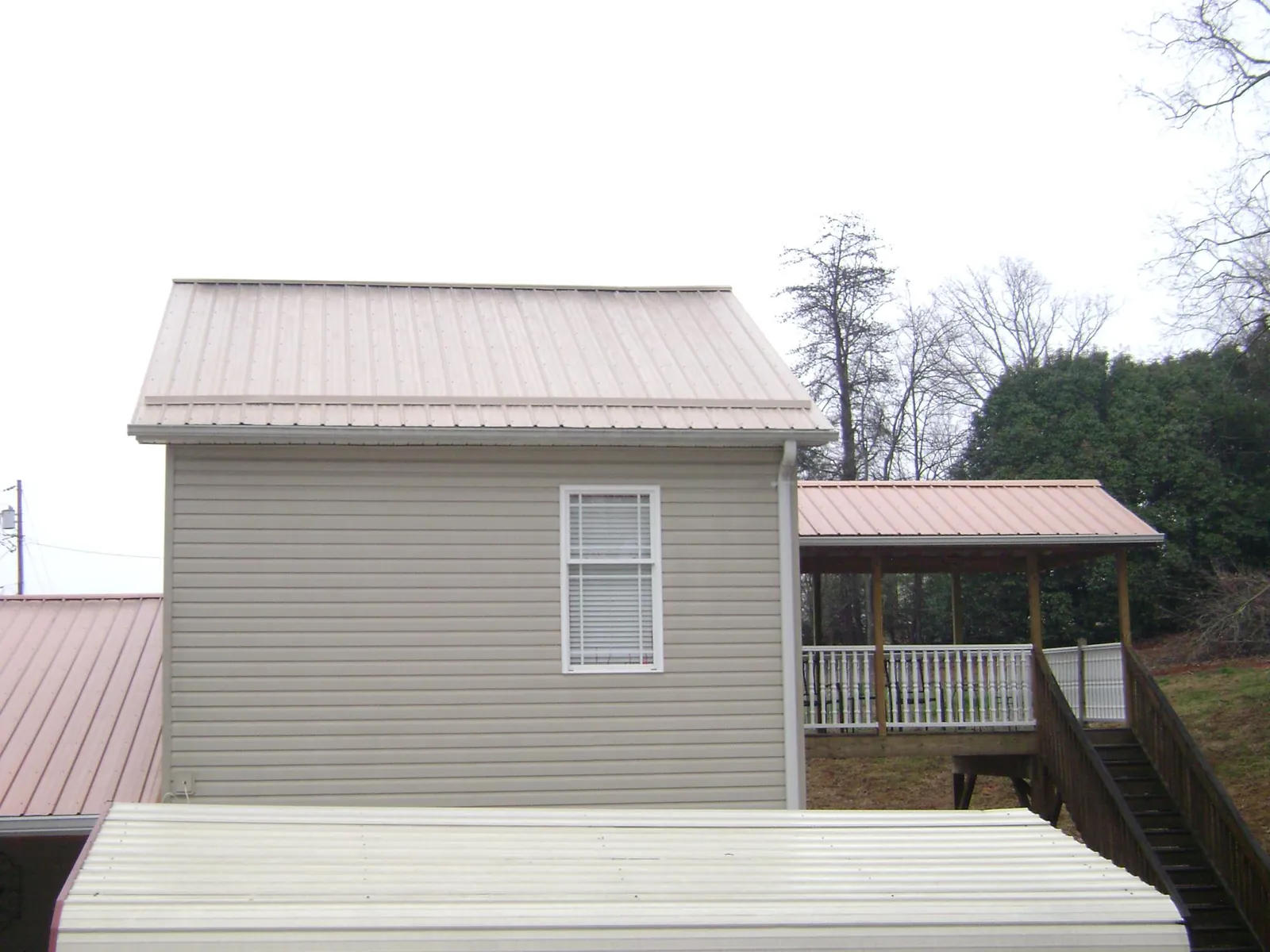 Tan metal roofs on a two story addition and attached porch, from a Roof Replacement job in Darien Center