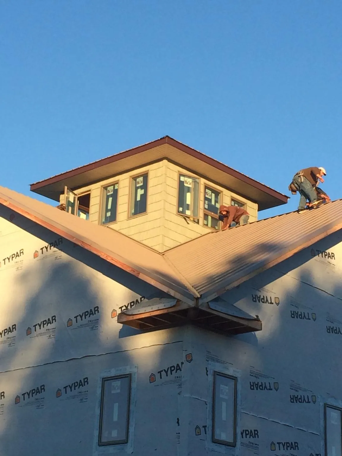 Roofers working around a rooftop cupola on a new metal roof at sunset — Roof Waterproofing in Darien Center by Roofing Brothers